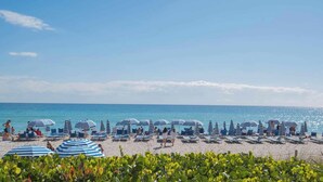 A beach with striped umbrellas and lounge chairs. - Beachwalk 1BR King Bed & Resort Access (Hallandale Beach)