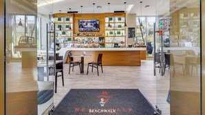 A bar area with a TV, shelves of bottles, and a counter. There are chairs and a table in the foreground. - Beachwalk 1BR King Bed & Resort Access (Hallandale Beach)