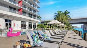 A poolside area with lounge chairs, a flamingo float, and umbrellas. - Beachwalk 1BR King Bed & Resort Access (Hallandale Beach)