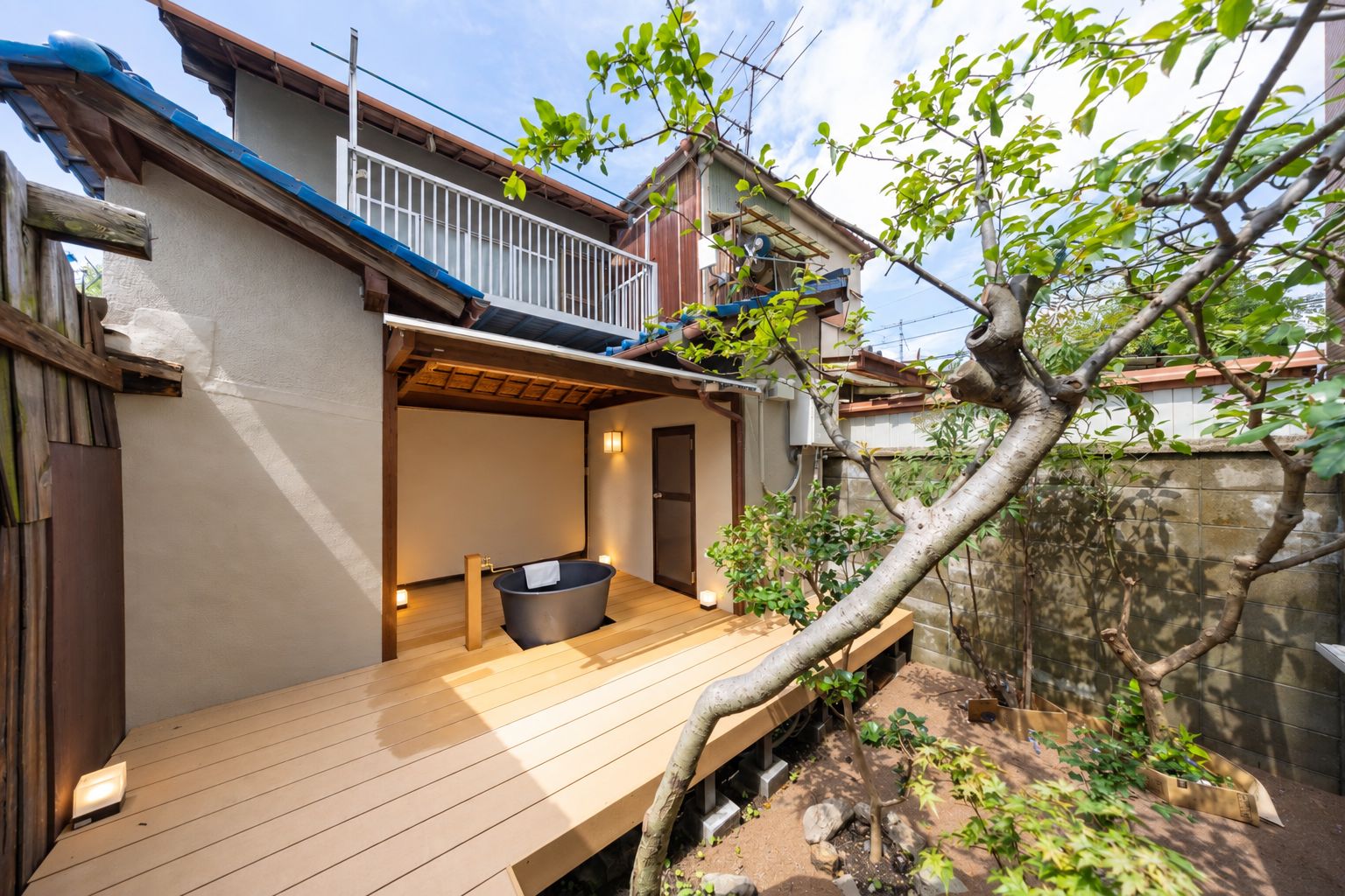 A wooden deck with a hot tub, a small enclosed area with a door, and a tree in the background.