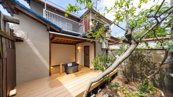 A wooden deck with a hot tub, a small enclosed area with a door, and a tree in the background.