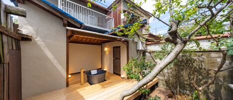 A wooden deck with a hot tub, a small enclosed area with a door, and a tree in the background.
