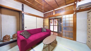 A traditional Japanese room with tatami flooring, a red sofa, a small wooden table, and shoji screens.