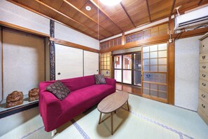 A traditional Japanese room with tatami flooring, a red sofa, a small wooden table, and shoji screens.