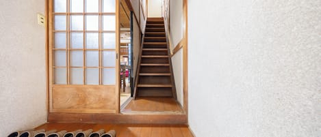 Una escalera de madera que conduce a una habitación con una puerta corredera, un banco de madera con zapatillas y vistas a otra habitación con muebles.