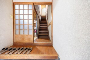 A wooden staircase leading to a room with a sliding door, a wooden bench with slippers, and a view of a room with furniture.