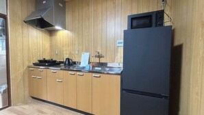 A kitchen with wooden cabinets, a black refrigerator, a stove, and a microwave. - Hakugetsu (Nara)