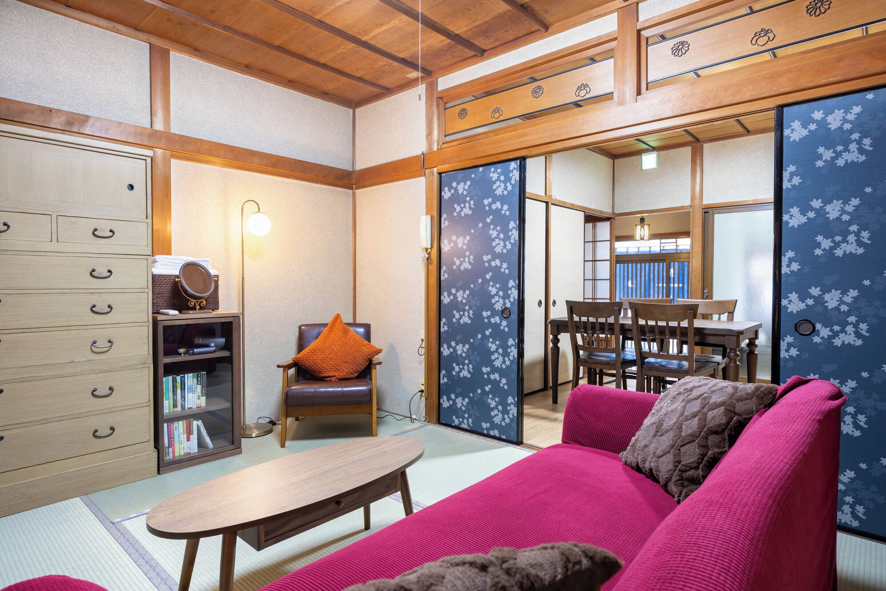 A traditional Japanese-style room with tatami flooring, a low wooden table, a sofa with cushions, a bookshelf, and sliding doors with floral patterns.