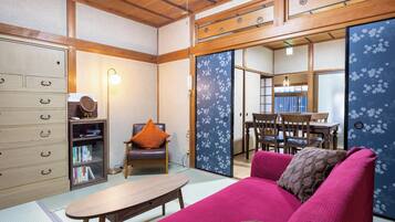 A traditional Japanese-style room with tatami flooring, a low wooden table, a sofa with cushions, a bookshelf, and sliding doors with floral patterns.