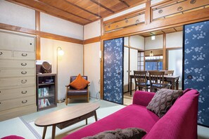 Une pièce de style japonais traditionnel, avec un sol recouvert de tatamis, une basse table en bois, un canapé avec des coussins, une bibliothèque et des portes coulissantes ornées de motifs floraux.