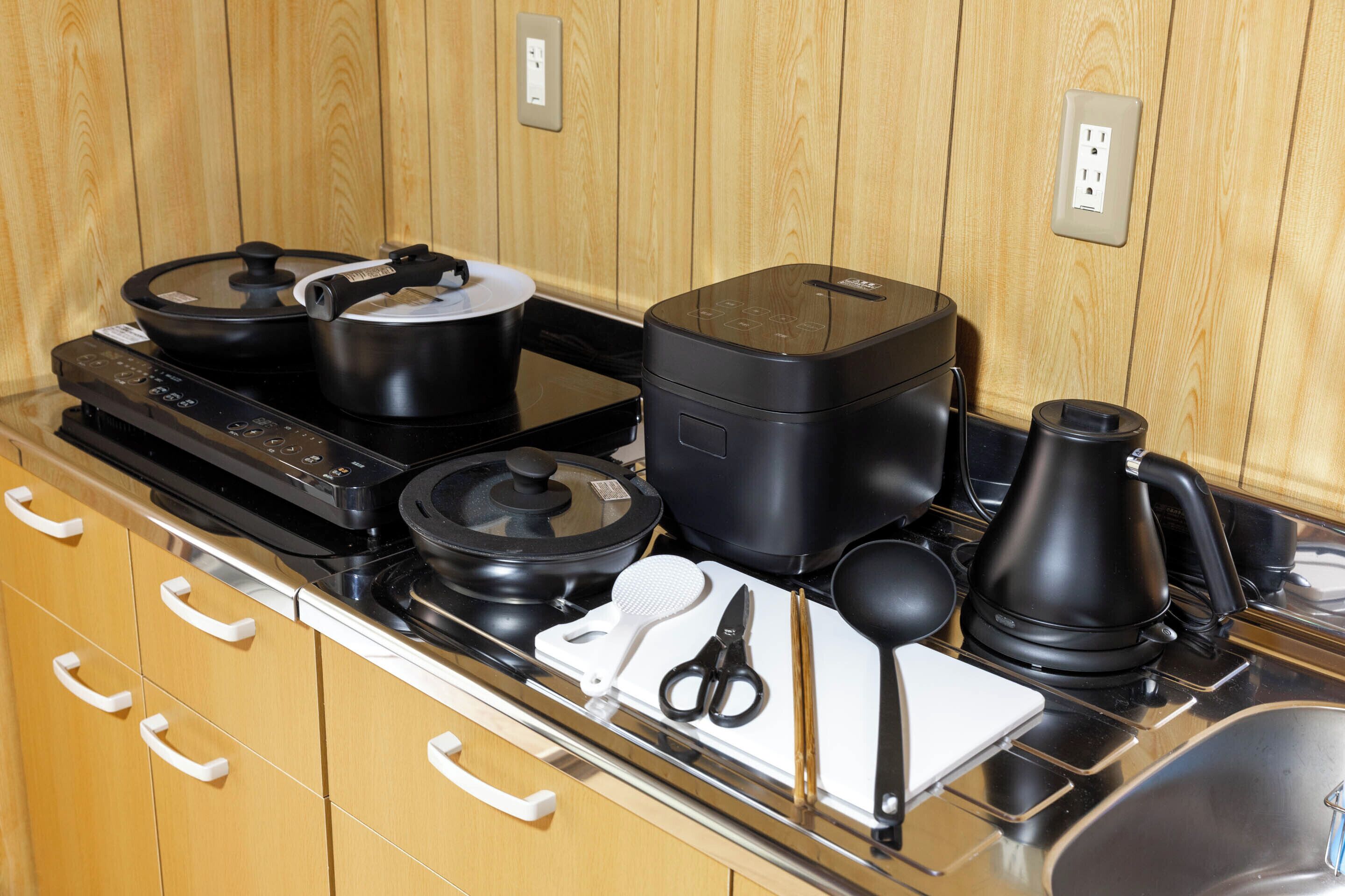 Una cocina con armarios de madera, estufa, ollas, hervidor y diversos utensilios.