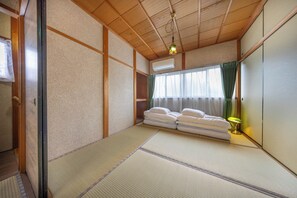 Una habitación japonesa tradicional con suelo de tatami, futón, celosía de papel shoji y una lámpara colgante.