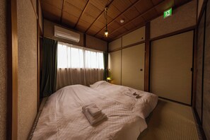 Une chambre d’hôtel comprenant un lit, une fenêtre avec des rideaux, un appareil de climatisation, un luminaire fixé au mur et une porte coulissante.
