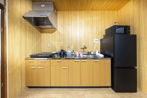 Una cocina compacta con armarios de madera, un refrigerador negro, una estufa y un microondas.