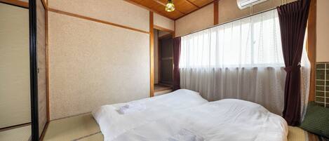 A hotel room with a wooden ceiling, a bed with white bedding, a futon, a futon with a green cushion, and a window with curtains.