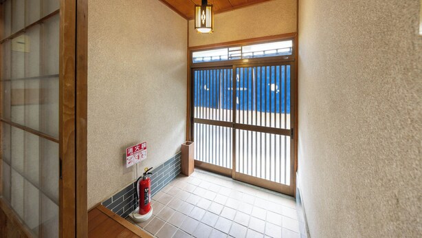 A corridor with a fire extinguisher, a fire exit sign, and a view through a sliding door. - Hakugetsu (Nara)