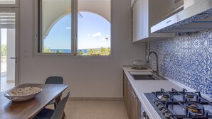 A modern kitchen with a view of the sea, a dining table with a bowl, and a stove. - Apartment 'Baia Dei Sogni - Aqua' with Sea View, Wi-Fi and Air Conditioning (Patù)