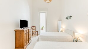 A hotel room with two beds, a television on a wooden cabinet, a small table with a lamp, and a large mirror on the wall. - Apartment 'Baia Dei Sogni - Aqua' with Sea View, Wi-Fi and Air Conditioning (Patù)