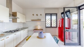 Cozinha moderna com armários brancos, fogão a gás, geladeira vermelha e janela com vista.