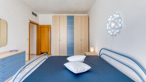 Quarto com cama, cômoda, guarda-roupa e mesa de cabeceira com abajur.