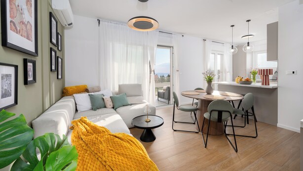 Una sala de estar moderna con sofá, mesa de comedor y sillas, un balcón con vistas, y una zona de cocina.