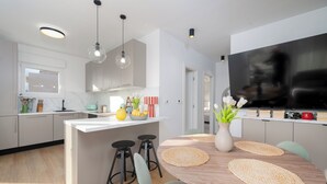 Una cocina moderna con una isla central, taburetes de bar, una mesa de comedor con individuales y un televisor de pantalla plana grande.