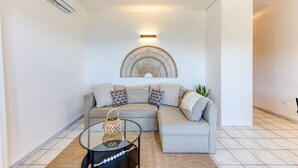 A modern living room with a sectional sofa, a glass coffee table, a wall-mounted light fixture, and a decorative wall piece. - Apartment 'Baia Dei Sogni - Petra' with Sea View, Wi-Fi and Air Conditioning (Patù)