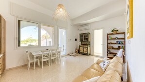 Zona d'estar espaiosa amb taula de dinar, sofà, prestatges i una làmpada penjant decorativa.