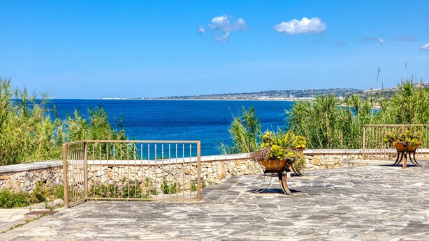 Terrassa d'un paviment de pedra amb plantes en testos i una reixa metàl·lica amb vista al mar.