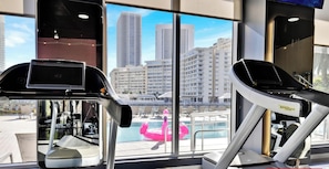 Une salle de sport équipée de matériel d’exercice et dotée d’une grande fenêtre offrant une vue sur la ville.