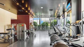 Ein Fitnessstudio mit Laufbändern, Krafttrainingsgeräten und einem großen Fenster mit Blick ins Freie.