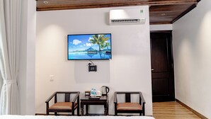 A hotel room with a bed, two chairs, a small table with a water bottle and a coffee pot, a TV on the wall, and an air conditioning unit. - TAM COC HA ANH HOTEL (Nam Hoa Lu)