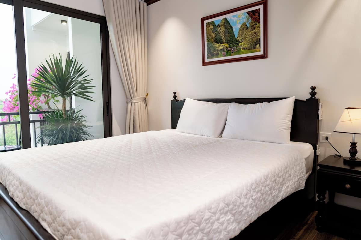 A neatly made bed with a quilted white bedspread, a dark wooden headboard, and a single bedside table with a lamp.