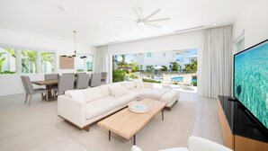A modern living room with a sectional sofa, a dining table with chairs, a flat-screen TV, and a balcony with a pool view.