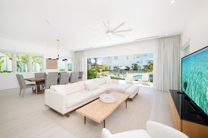 A modern living room with a sectional sofa, a dining table with chairs, a flat-screen TV, and a balcony with a pool view.