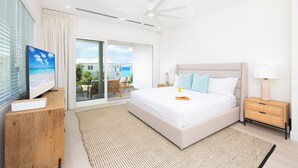 A modern bedroom with a large bed, a television, a ceiling fan, and a view of the outdoors.