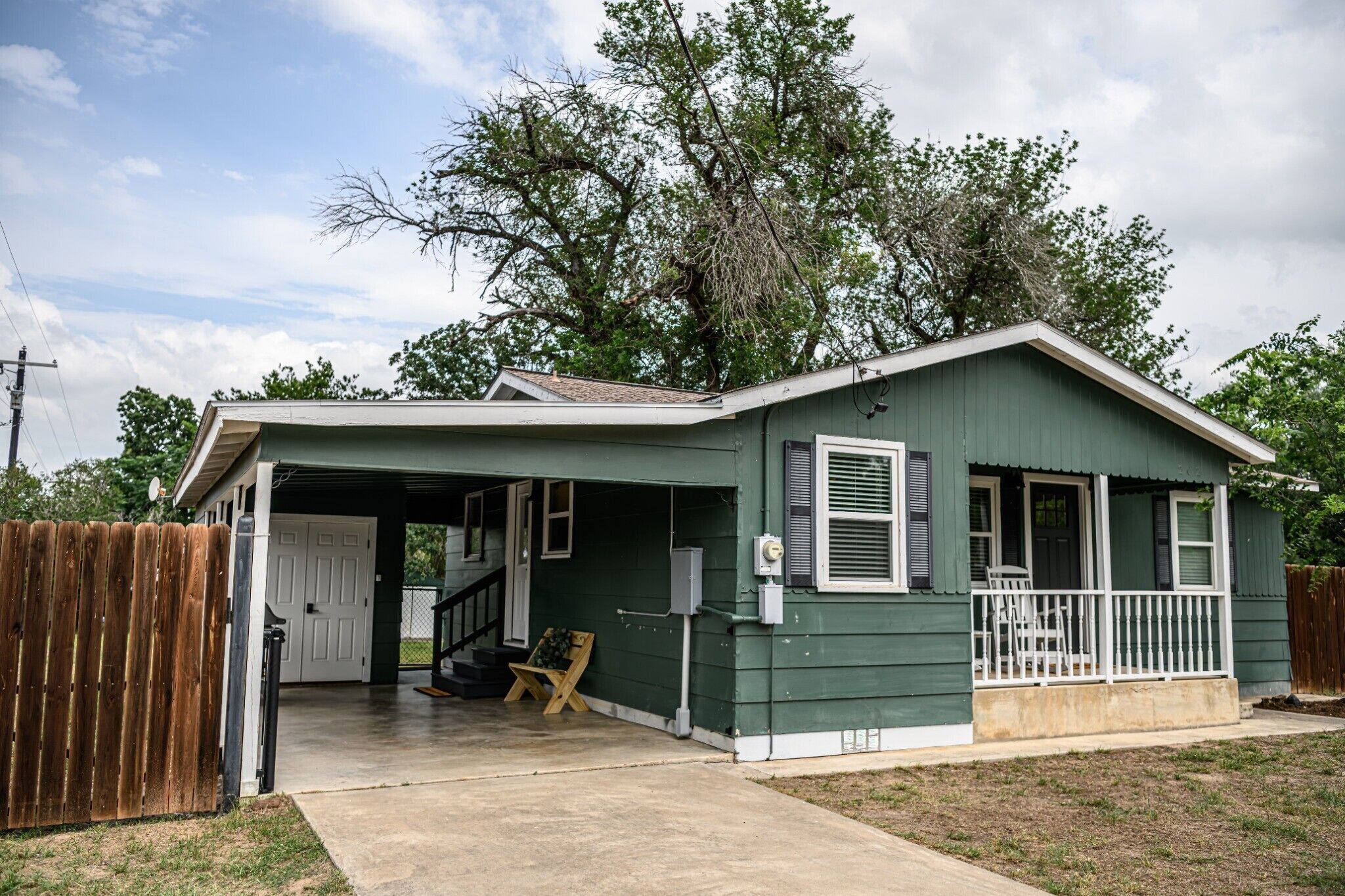 A green single-story house with a covered porch, a front door, and a staircase leading to the entrance.