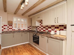 A kitchen with wooden beams, white cabinets, a checkered backsplash, and a wooden floor. - Wick Cottage (Whitby)