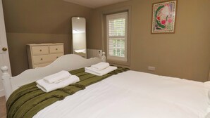 Ein Schlafzimmer mit Bett, Kommode, Spiegel, Fenster und einem Gemälde.