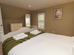 Ein Schlafzimmer mit Bett, Kommode, Spiegel, Fenster und einem Gemälde.