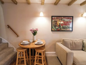 Ein Essbereich mit einem Holztisch, vier Hocker, einer Blumenvase und einem Poster an der Wand.