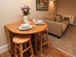 A dining area with a wooden table, white plates, bowls, and cutlery. There is a vase with flowers on the table. A beige sofa is in the background. - Wick Cottage (Whitby)