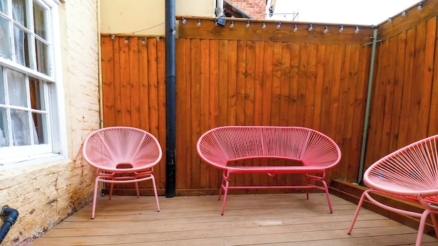 Eine Holzterrasse mit drei rosa Stühlen und einem Holzzaun.