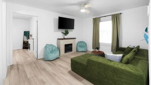 Un salon moderne avec un canapé vert, deux fauteuils poire, une cheminée, un téléviseur à écran plat et un ventilateur de plafond.