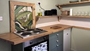 Una cucina con piano di lavoro in legno, forno, frigorifero e mensole piene di stoviglie e bicchieri.