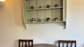 Un'area pranzo con un tavolo rotondo e due sedie imbottite, una mensola verde a parete con oggetti decorativi e un tappeto con trama.