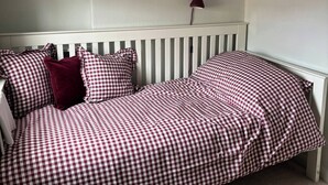Camera da letto con copriletto a quadri, una testiera bianca e una lampada a parete.