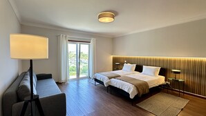 Hotelkamer met twee bedden, een bureau, een lamp en uitzicht op groen buiten het raam.