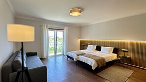 A hotel room with two beds, a desk, a lamp, and a view of greenery through the window. - Águia | Private Pool | 10 Pax | Albufeira (Albufeira)