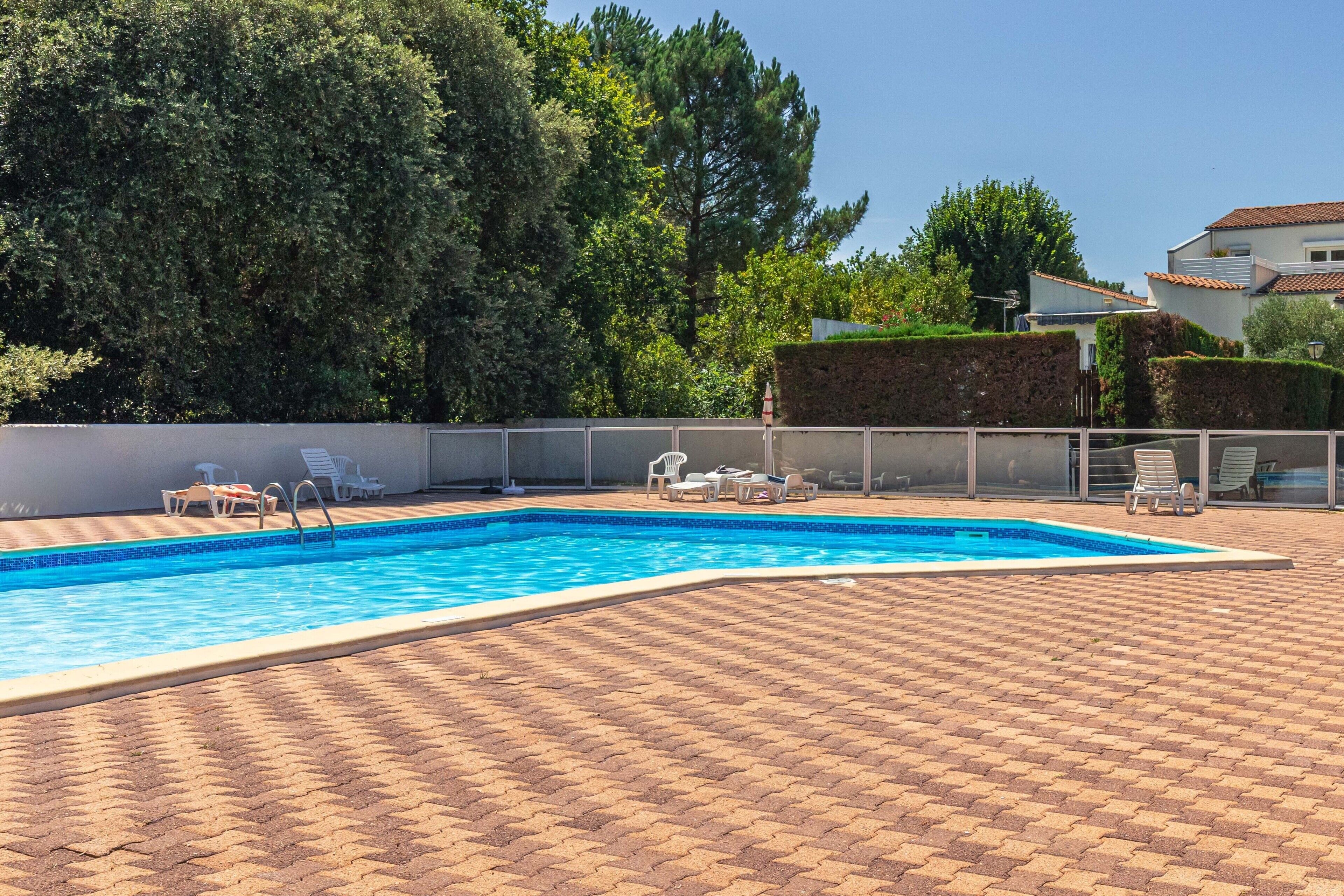 A rectangular swimming pool with a tiled edge, surrounded by a paved patio with interlocking bricks.